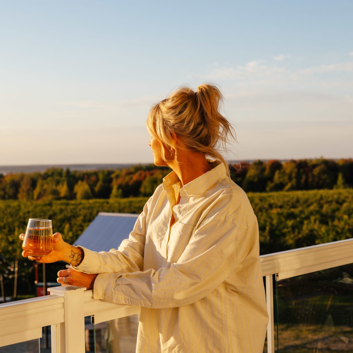 Femme tenant un verre en train de regarder l'horizon sur un terrasse. 