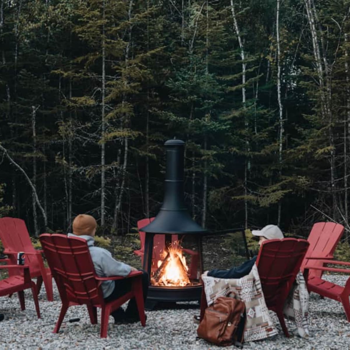 Personnes assises sur des chaises Adirondack rouges autour d'un foyer extérieur. 