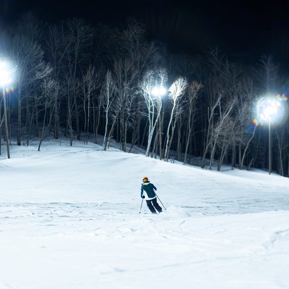 Personne seule en train faire du ski alpin en soirée sur une piste éclairée.