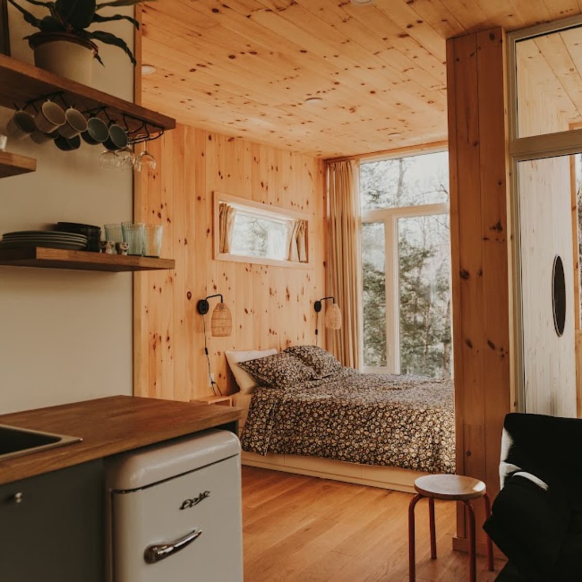 Intérieur d'un mini-chalet; ses murs sont faits de bois naturel et le lit est placé devant une grande fenêtre.
