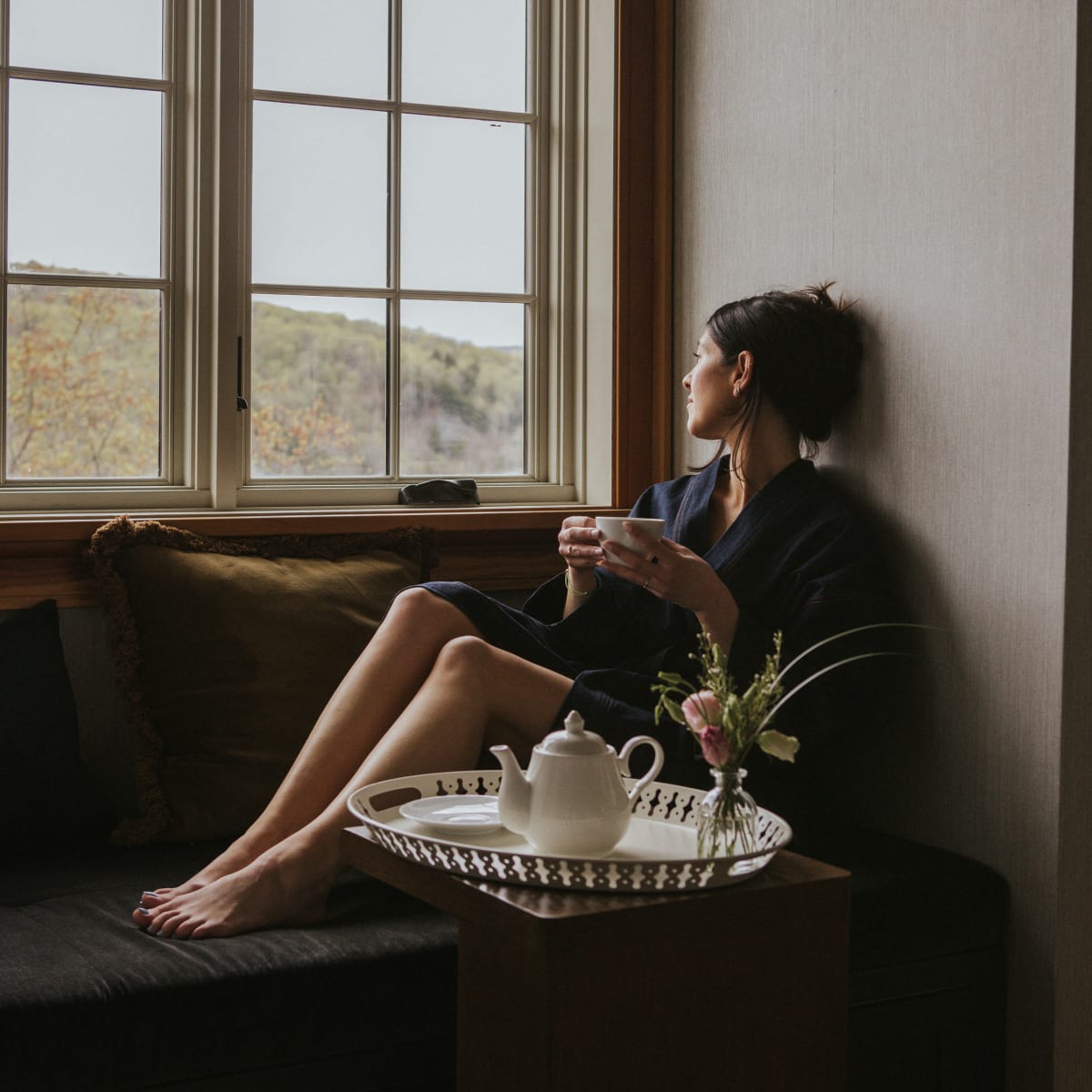 Femme relaxant devant une fenêtre avec un thé.