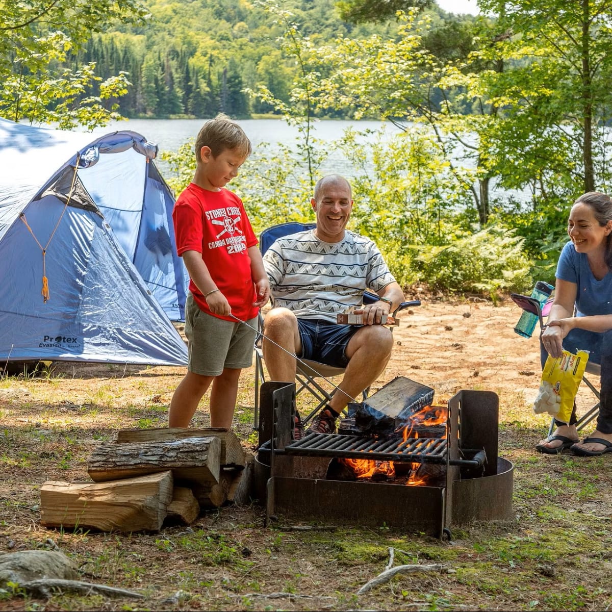 Terrain de camping avec une tente, un garçon et ses parents.