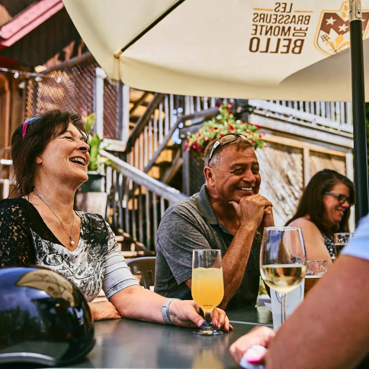 People sitting at a table on a terrace with umbrellas, having a drink.