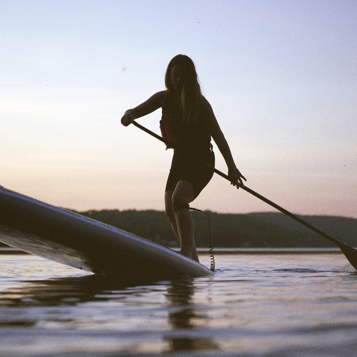 A woman on a stand-up paddleboard in the evening.