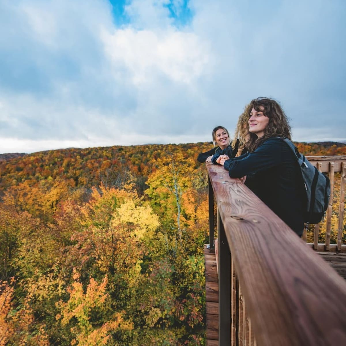 3 women hiking and admiring the fall view from a lookout at Parc des Montagnes Noires de Ripon.