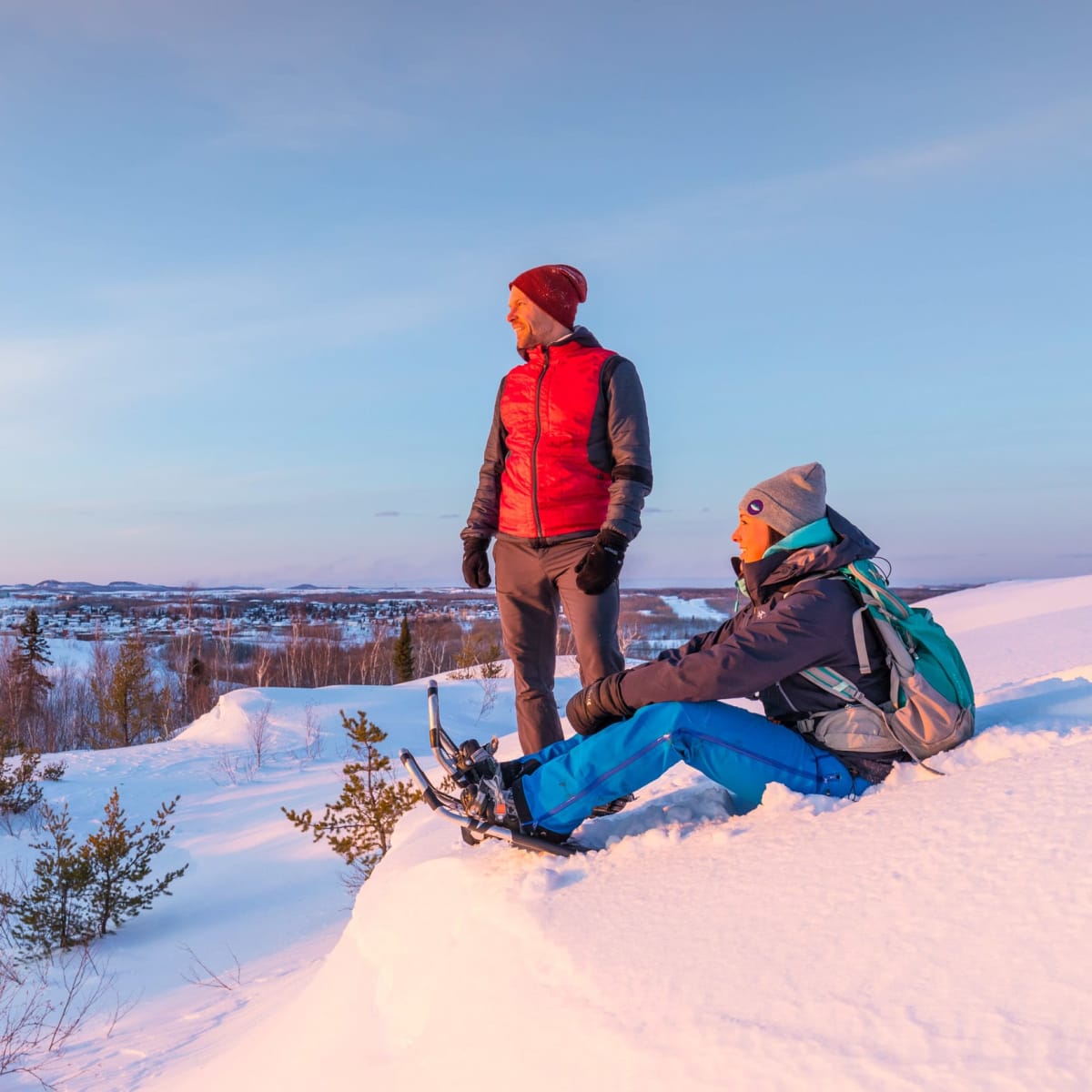 Two hikers in winter looking out over the landscape from a mountaintop.