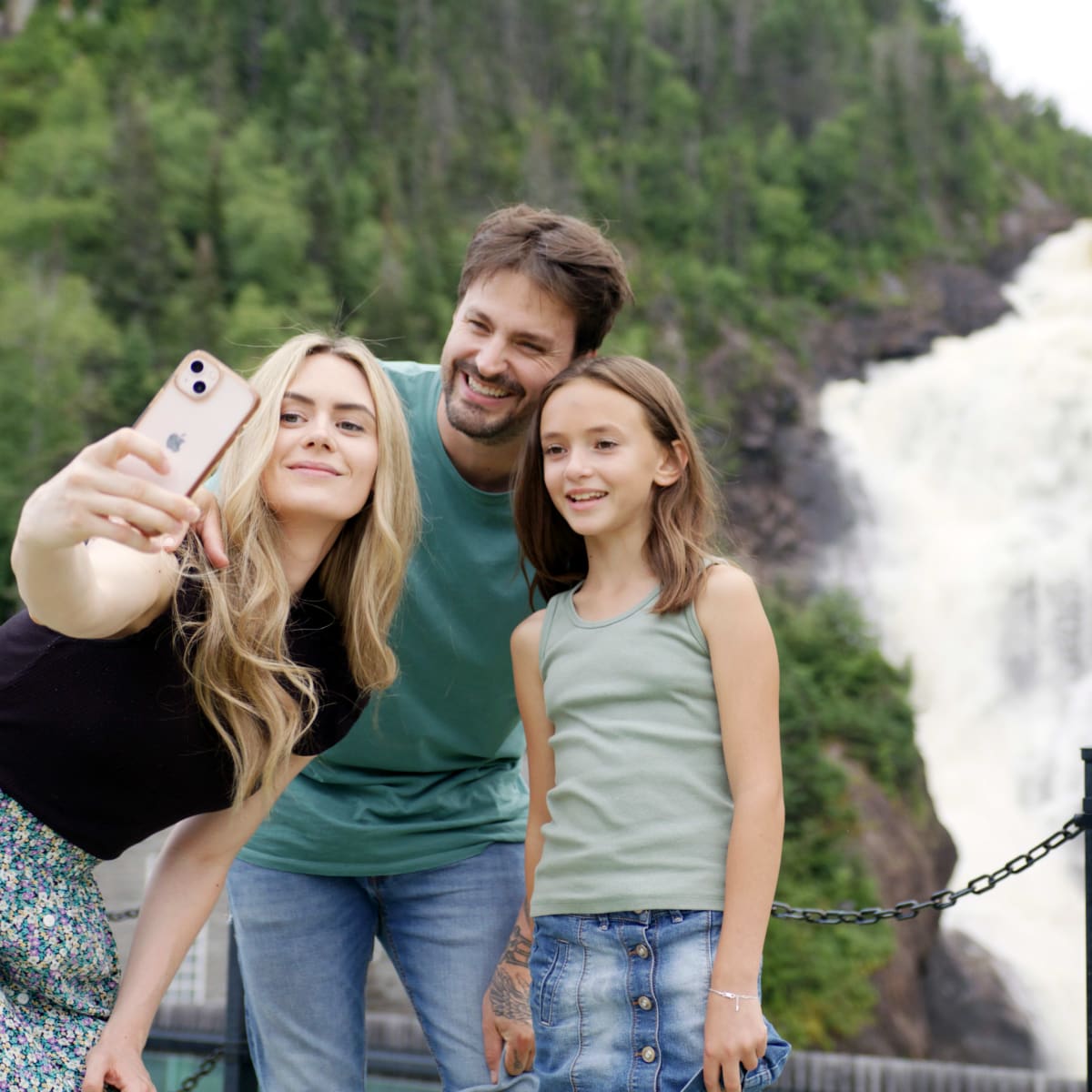 A family taking a photo with a waterfall in the background at the Val-Jalbert Historic Village.