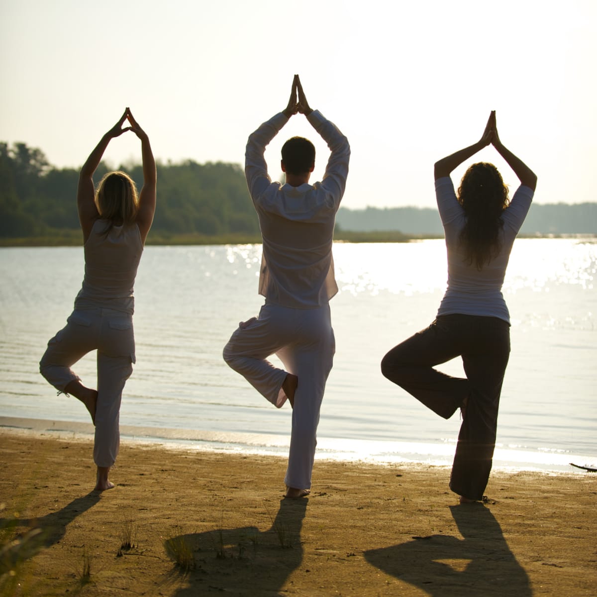 Three people doing yoga on the beach