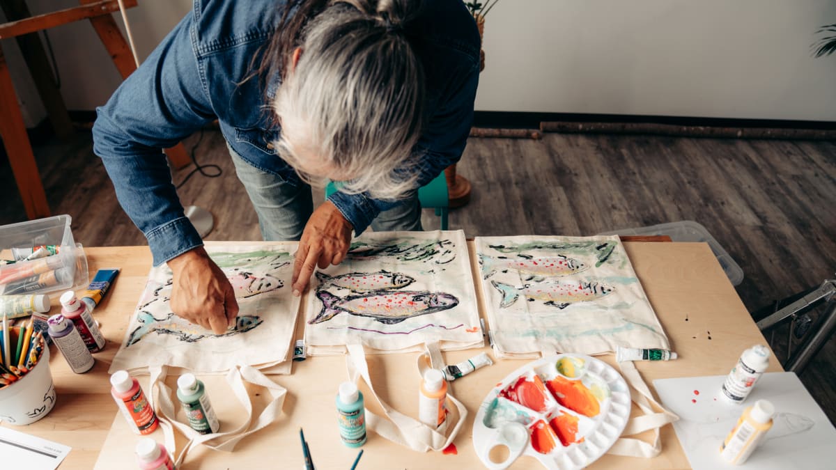 An Indigenous woman paints fish on a cloth