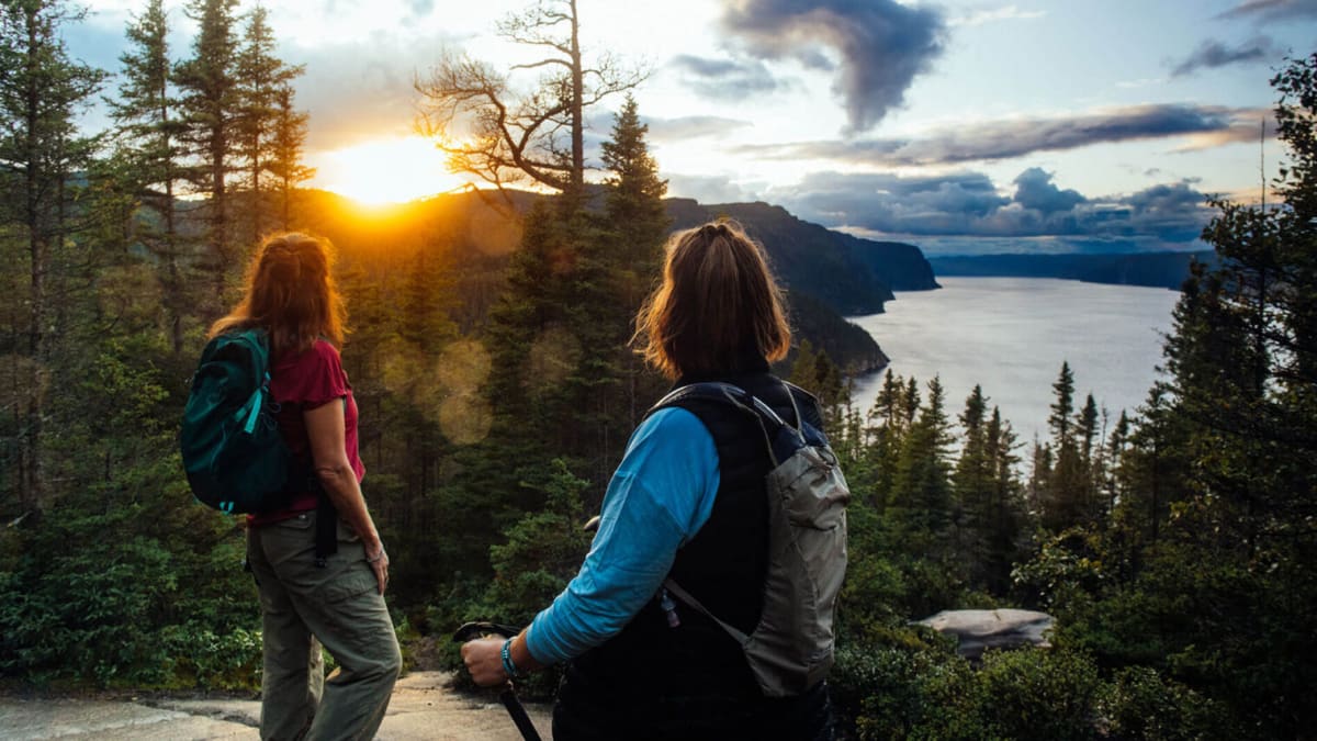 Parc national du Fjord-du-Saguenay - Two women on top of a mountain, forest and sunset in the background.