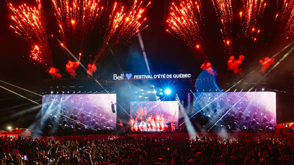 Crowd in front of an outdoor stage at night with fireworks.