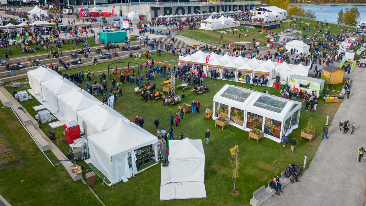 The Amphithéatre Cogeco in Trois-Rivières by the river, with kiosks and spectators on the grass.