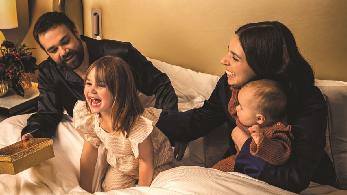 Two parents with a young daughter and a baby in a luxurious hotel bed.