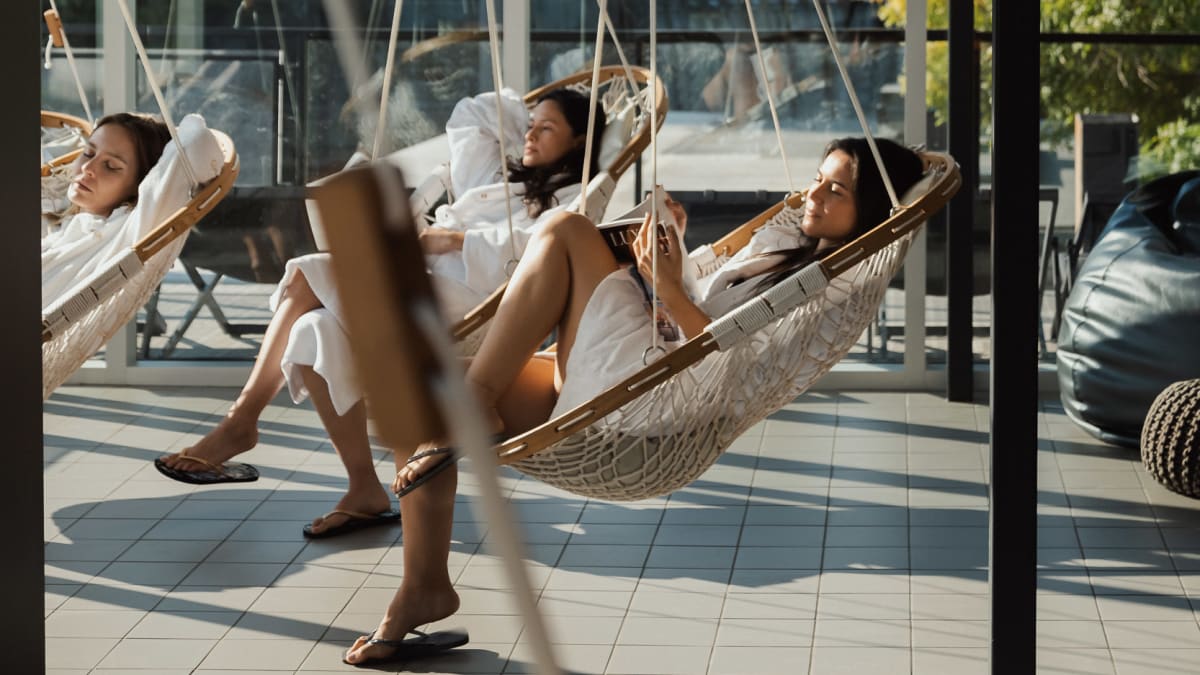 3 young women on the patio at the spa relaxing in hanging swing-chairs.