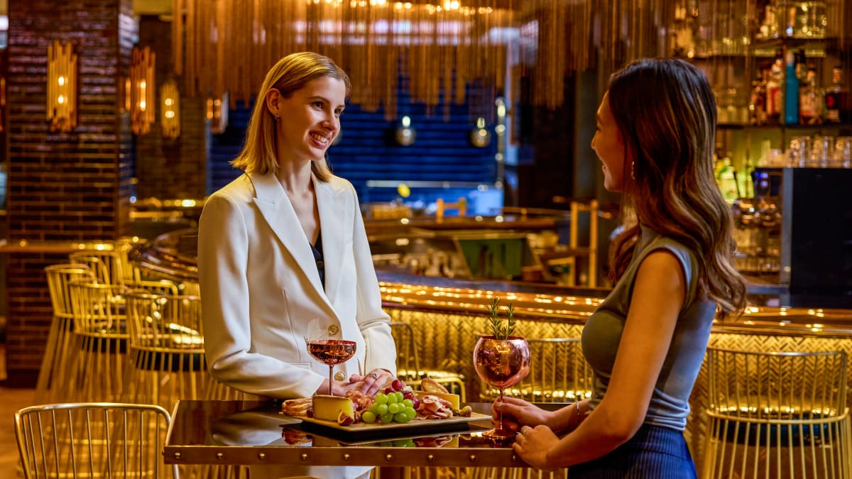 Two women enjoying a glass of red wine in a gold-accented dining venue.