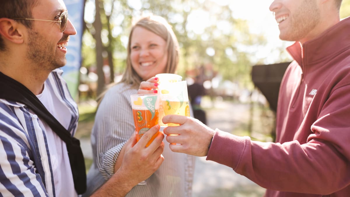 Three people making a toast with a glass of beer in hand.