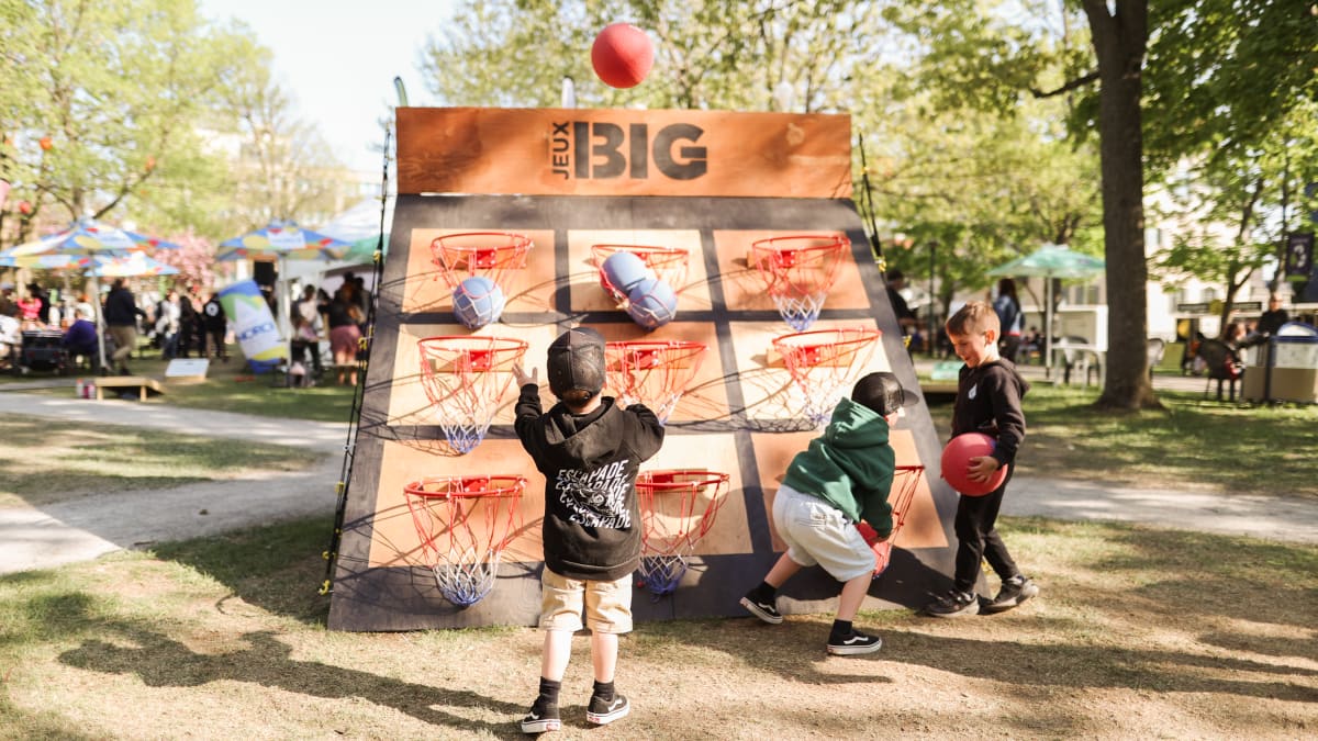 Children playing a giant game combining cornhole and basketball.