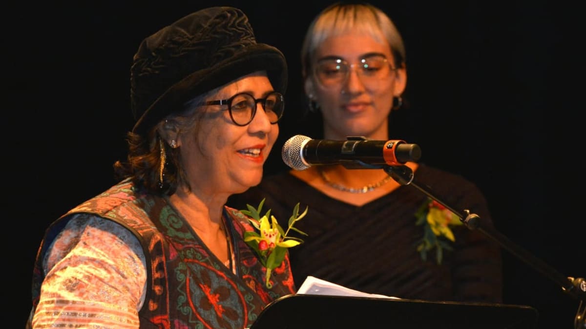 Une femme qui devant un micro et un podium récite un poem et une jeune femme se tient à côté d'elle.