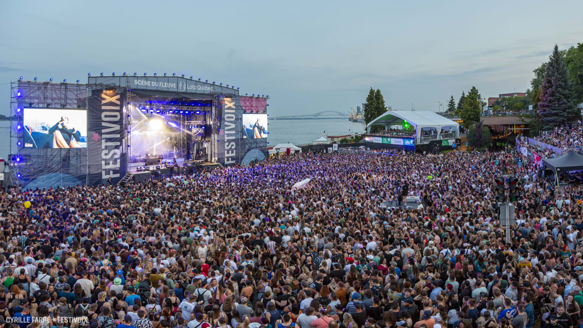 A dense crowd in front of a stage by the St. Lawrence River.