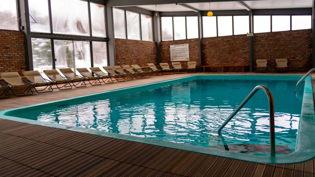 Indoor pool surrounded by chairs in a large room with windows.