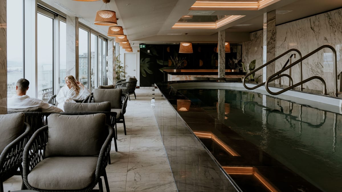 Deux personnes en peignoir assises près d’une piscine intérieure à l’ambiance zen; ils admirent la vue extérieure.