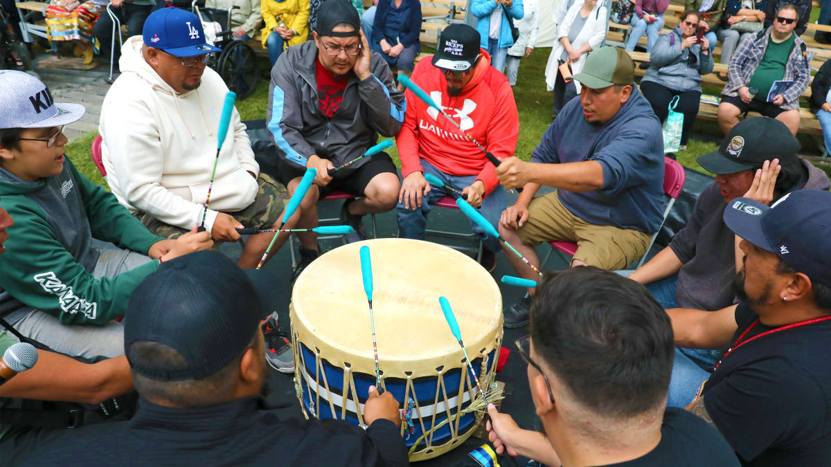 Group of people around a drum and spectators behind them.