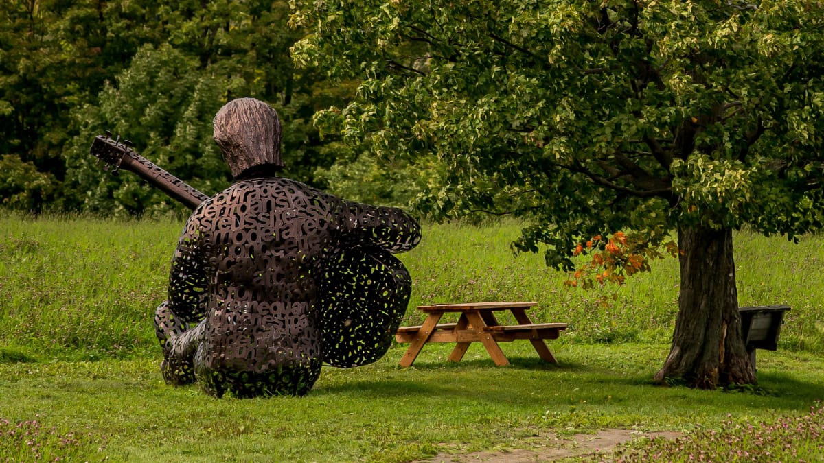 Sculpture représentant Félix Leclerc et paysage côtier de l'ile d'orléans.