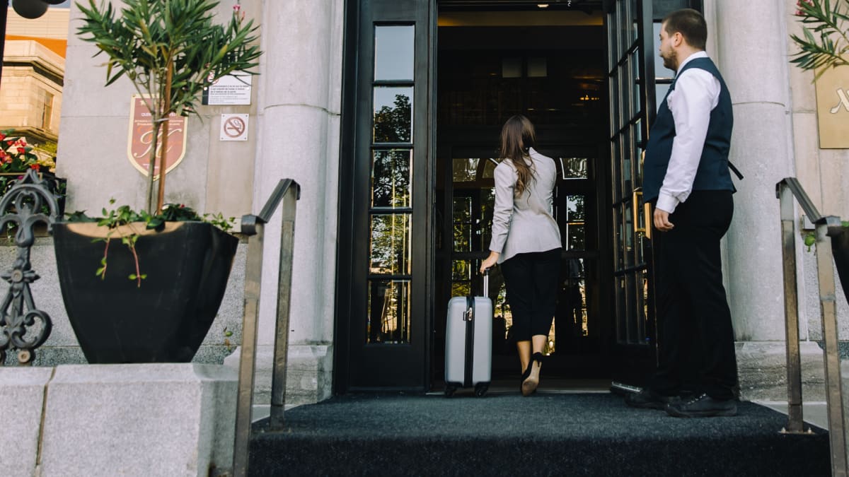Devanture de l'hôtel; une femme traverse la porte aux côtés d'un portier.