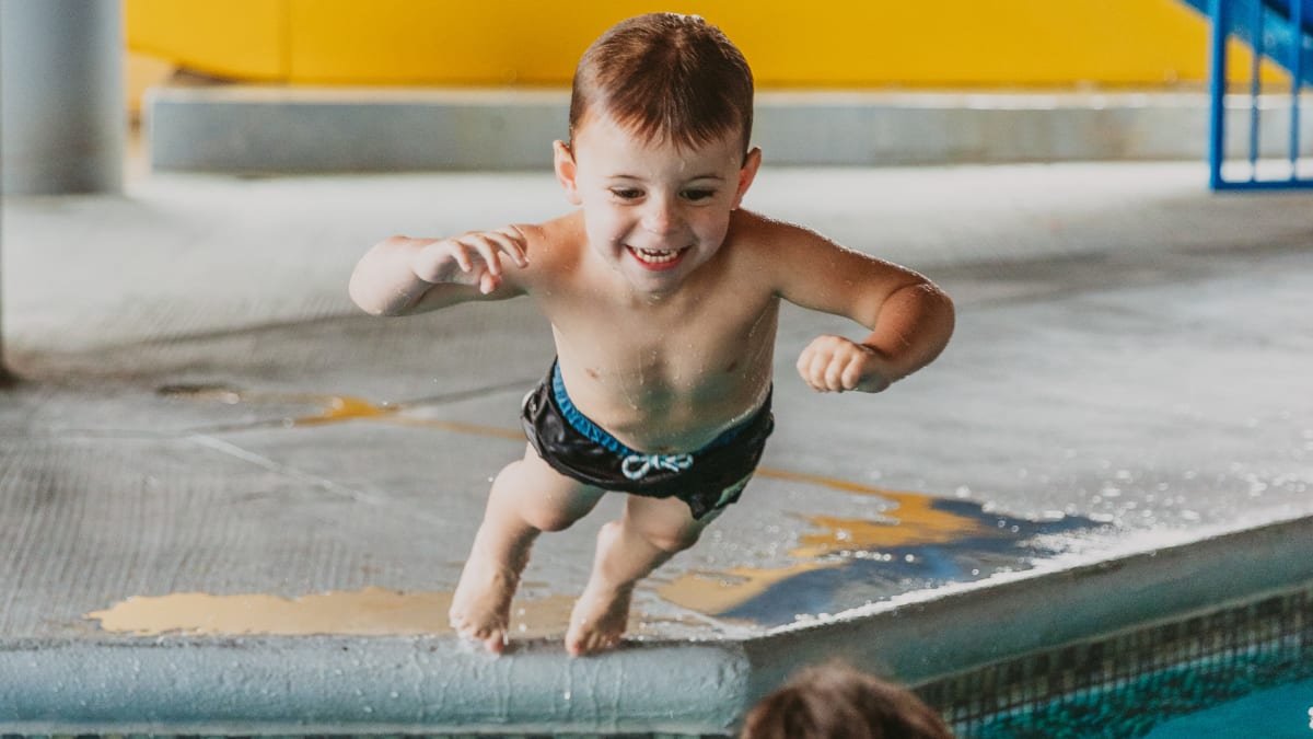 Mother in the hotel pool catching her son jumping in the water.