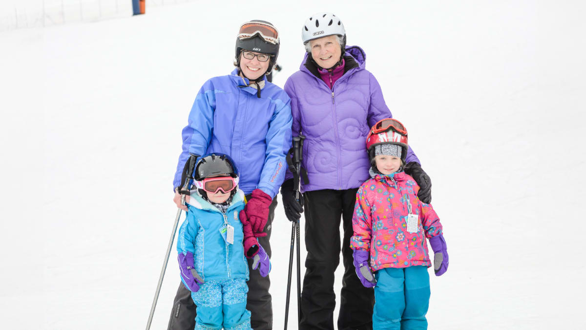 Mother, grandmother and two little girls in ski gear at the foot of the hill.