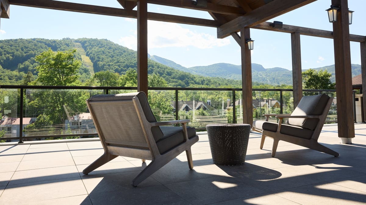 A covered outdoor terrace, featuring two comfortable chairs, overlooks a mountainous landscape.
