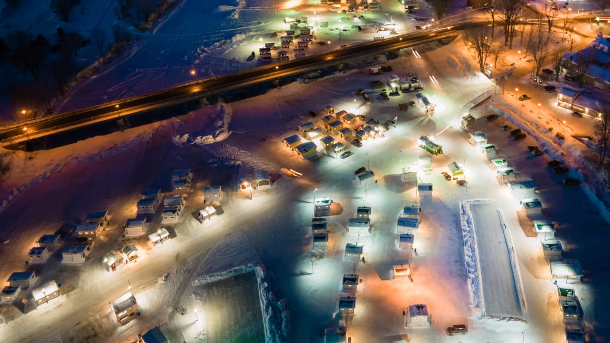 Village de pêche sur glace illuminé vu de haut dans la nuit.
