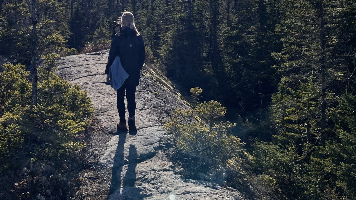 Woman on a trail at the top of a mountain under a bright sun.