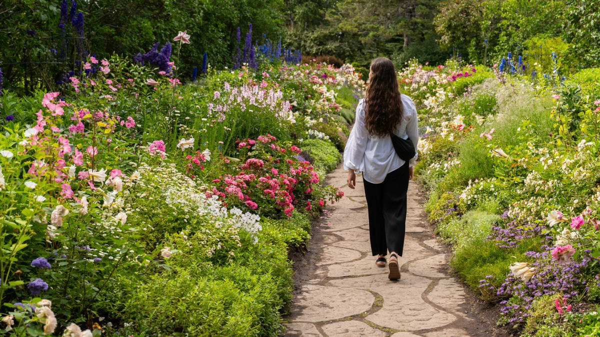 Femme qui marche qui traverse un jardin fleuri.