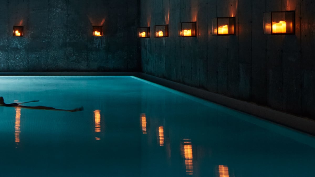 Piscine intérieure dans la pénombre, éclairée par une douce lumière; une femme se tient au bord de la piscine.