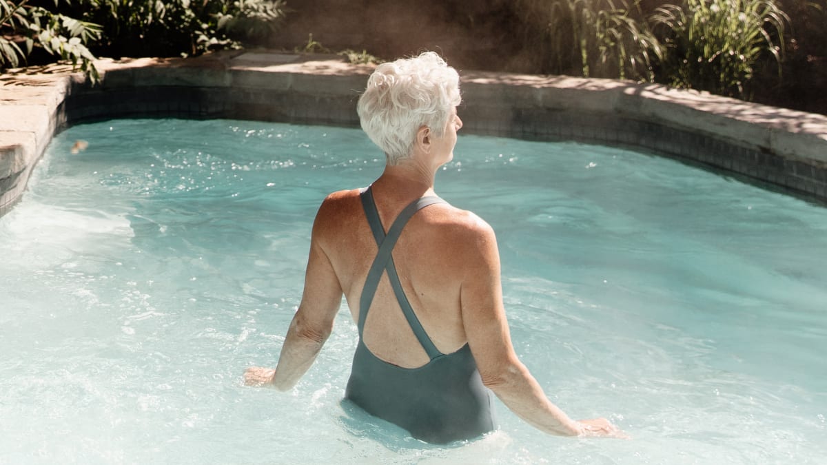 Femme dans un bain extérieur du spa; une chute d'eau alimente le bain.