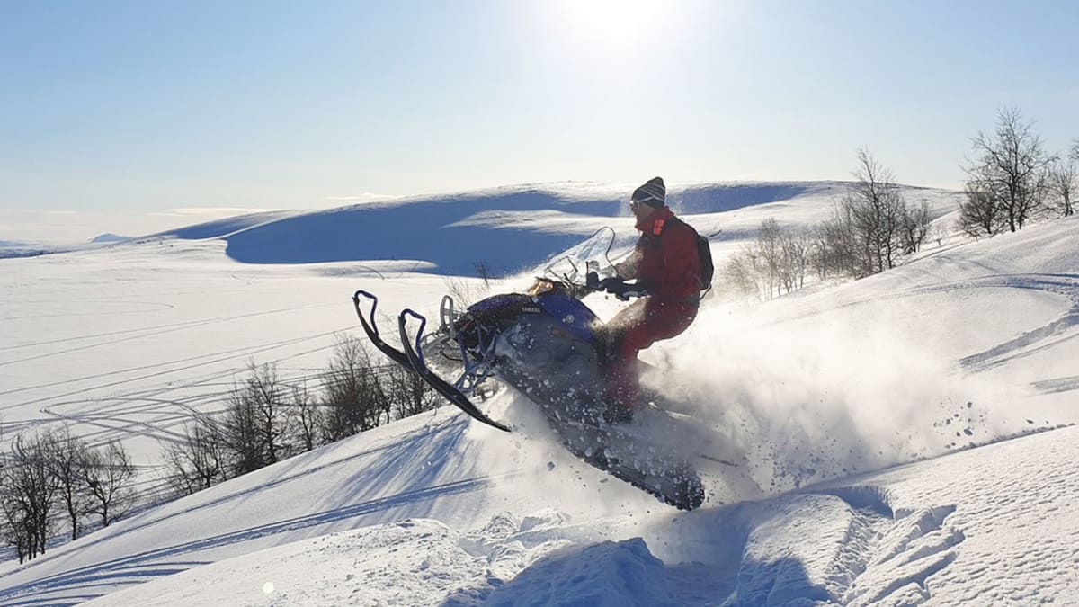 Person snowmobiling through a vast snow-covered landscape.