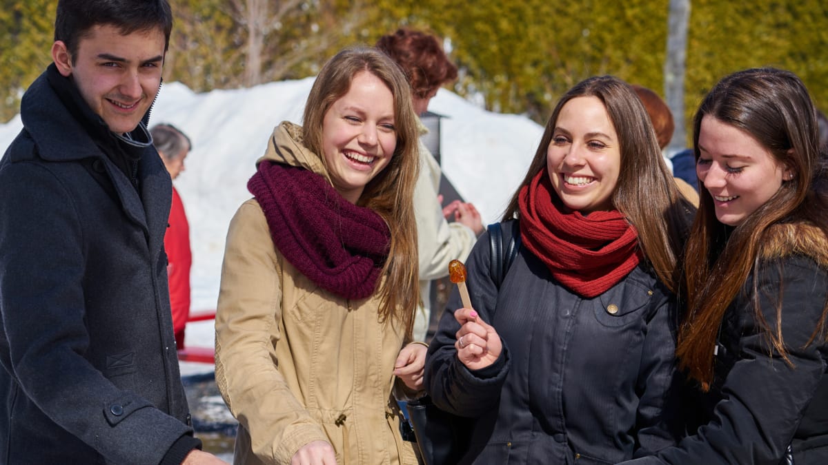 A man and three women all smiling as they enjoy taffy on snow.