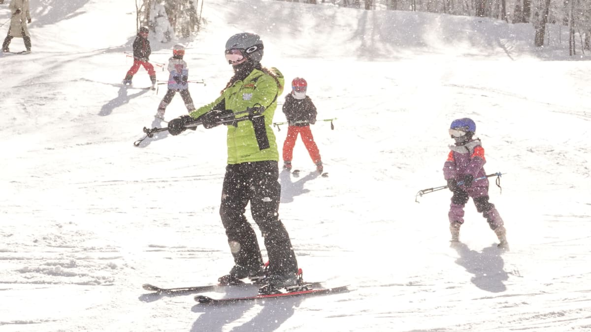 Moniteur de ski avec apprentis skieurs et skieuses derrière lui.