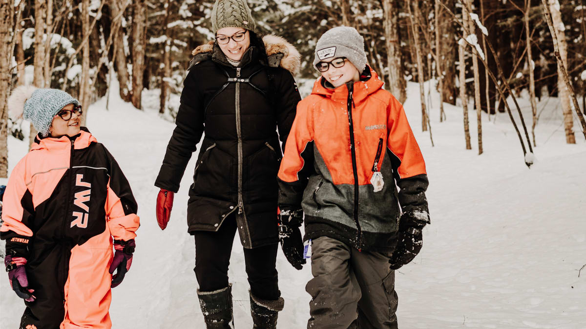 Une mère et deux enfants, tous souriants, dans une forêt enneigée.