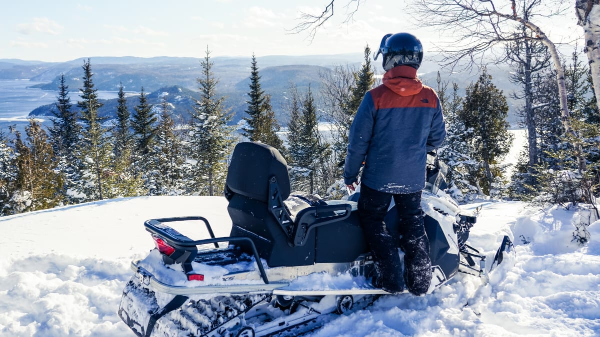 Snowmobiler looking out at the forest and river.