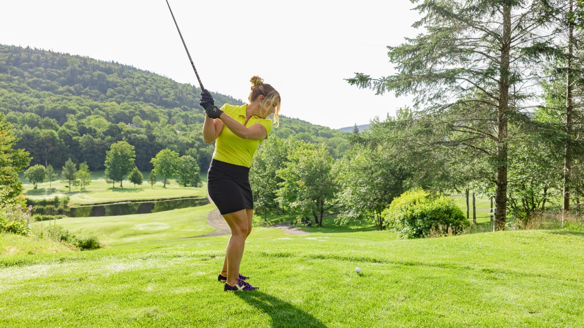 Woman on a golf course about to hit the ball.