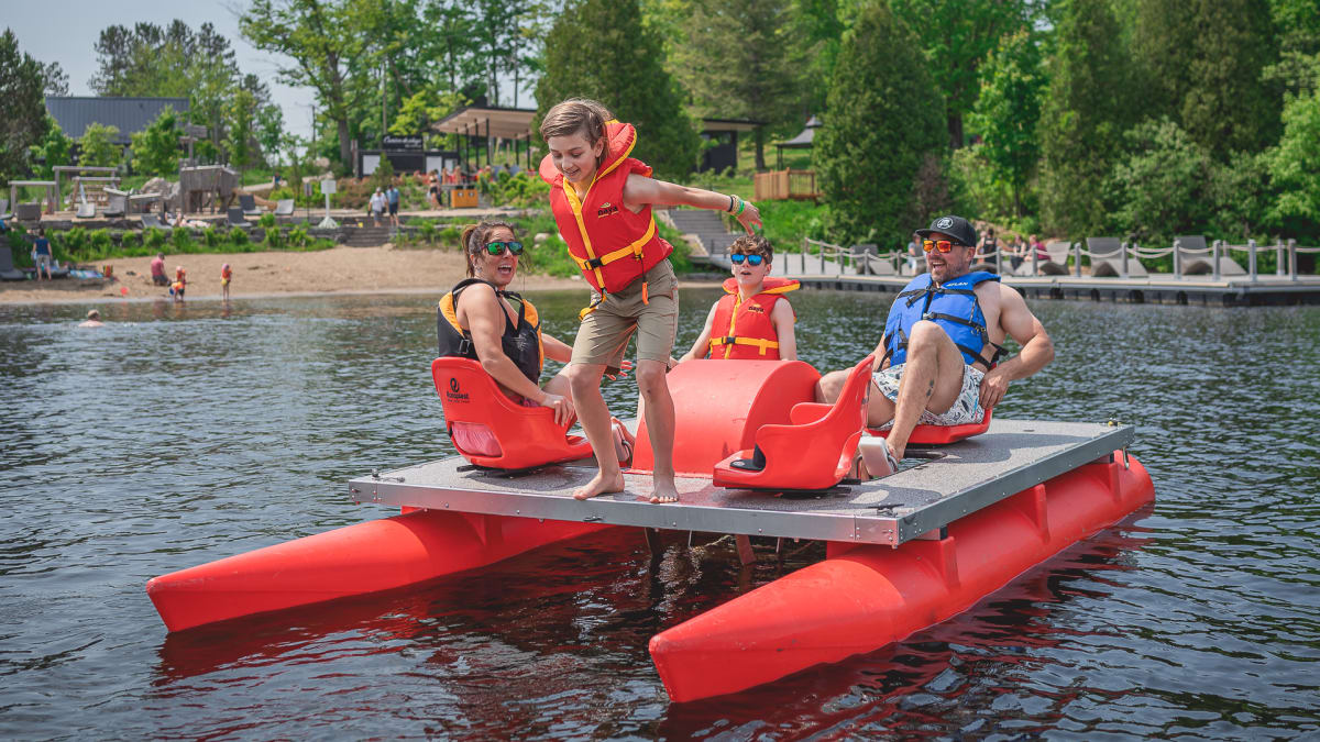 Family of four on a big pedal boat; a boy is about to jump into the lake.