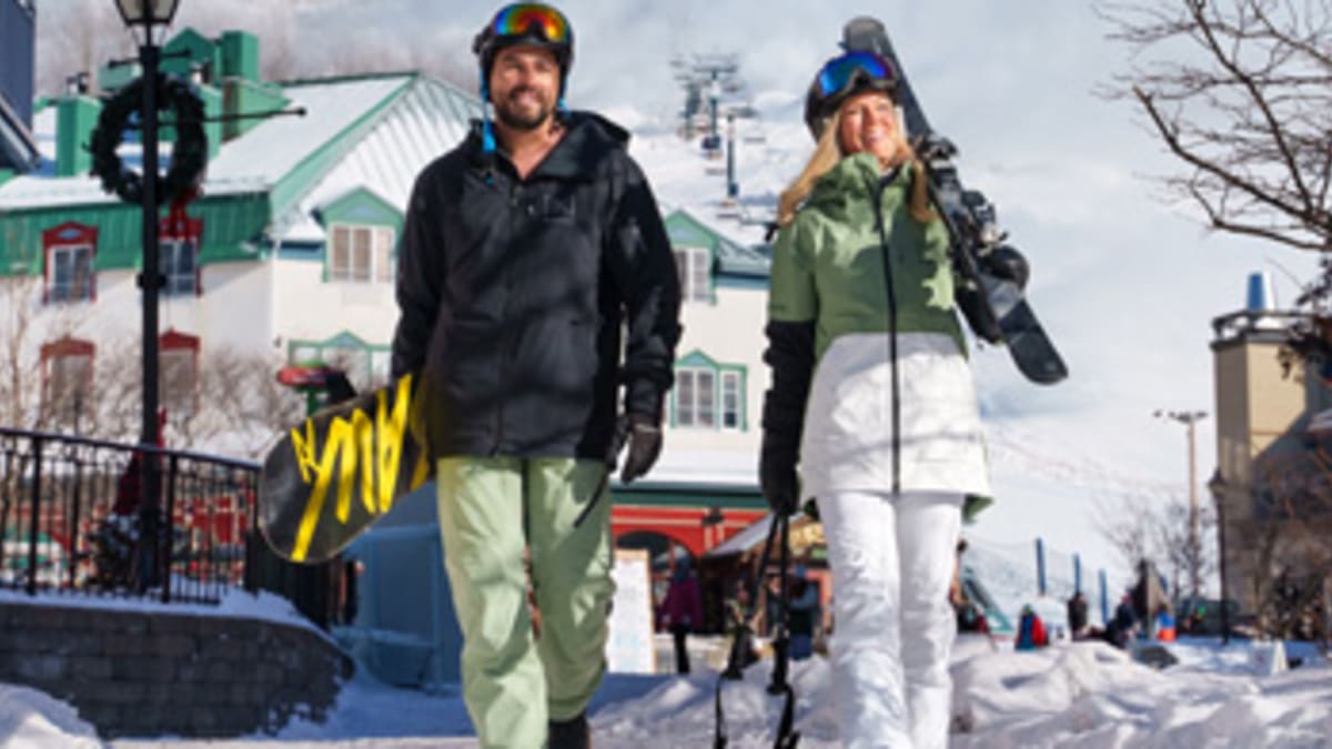 A man and a woman walking with their skiing and snowboarding equipment in Tremblant