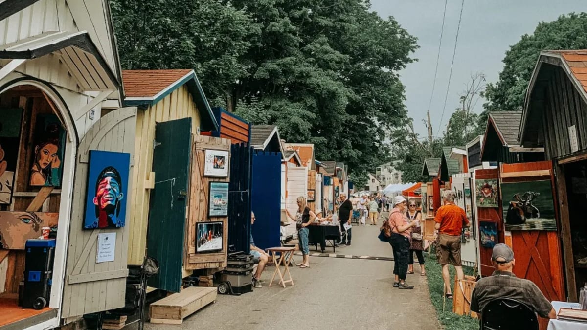 An alleyway lined with small cabins showcasing works of art.