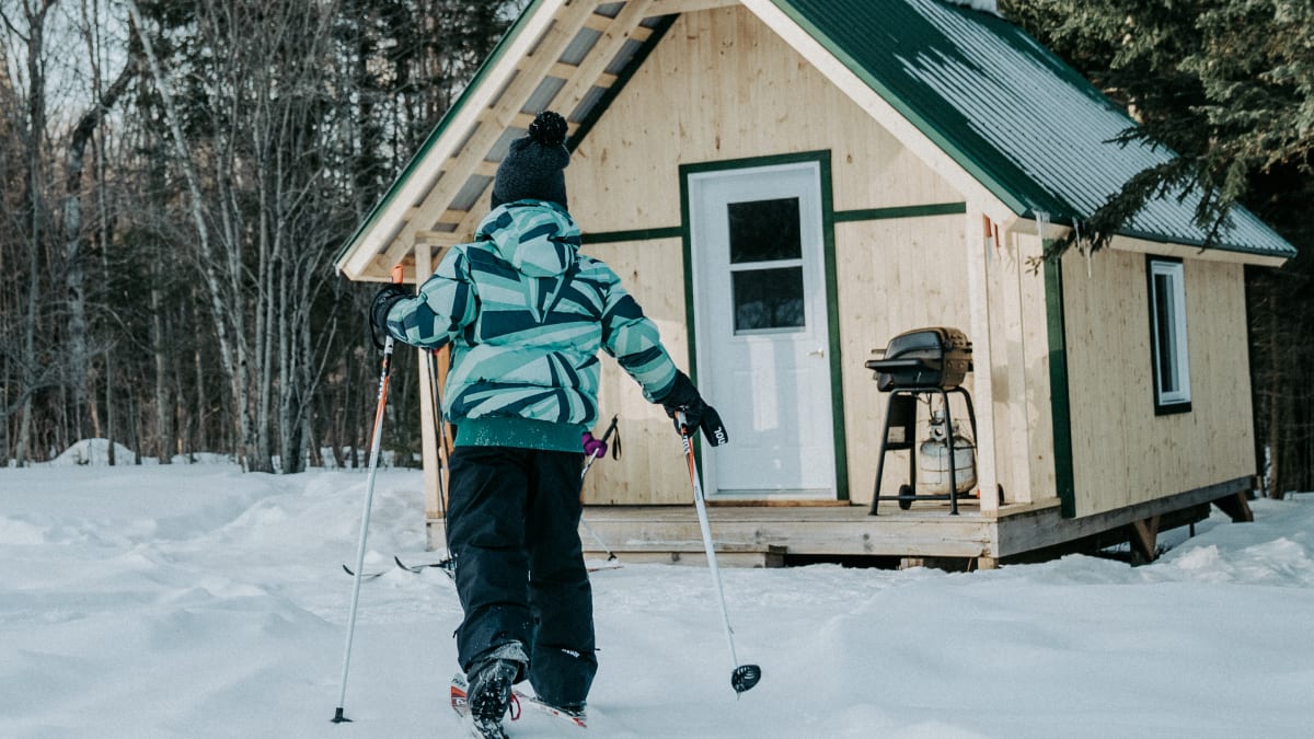 Child wearing skis returning to a cabin.