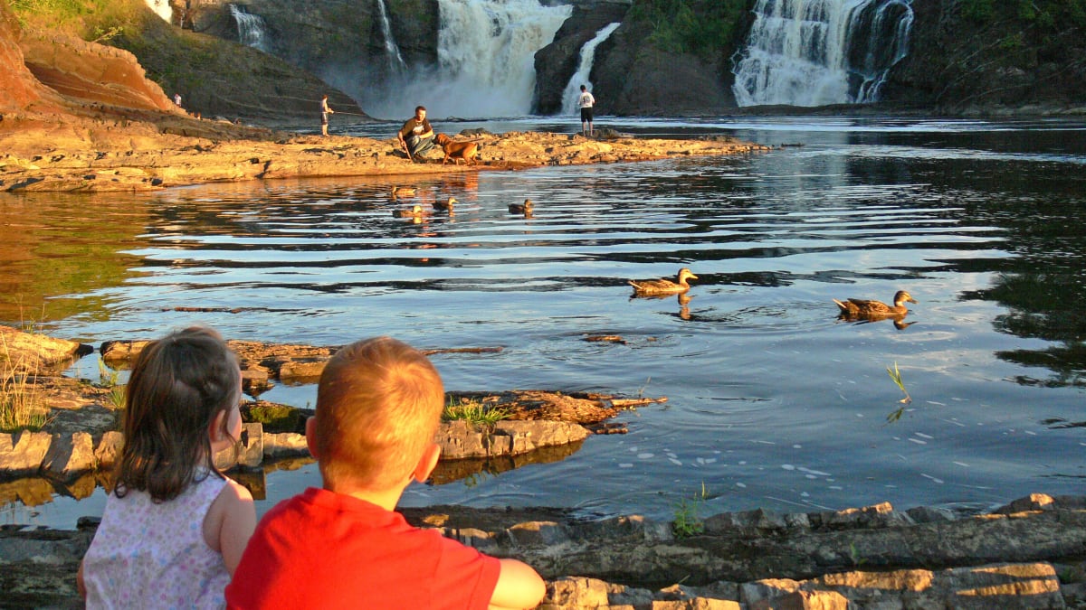 Two young kids sitting by the water at Parc des Chutes-de-la-Chaudière.