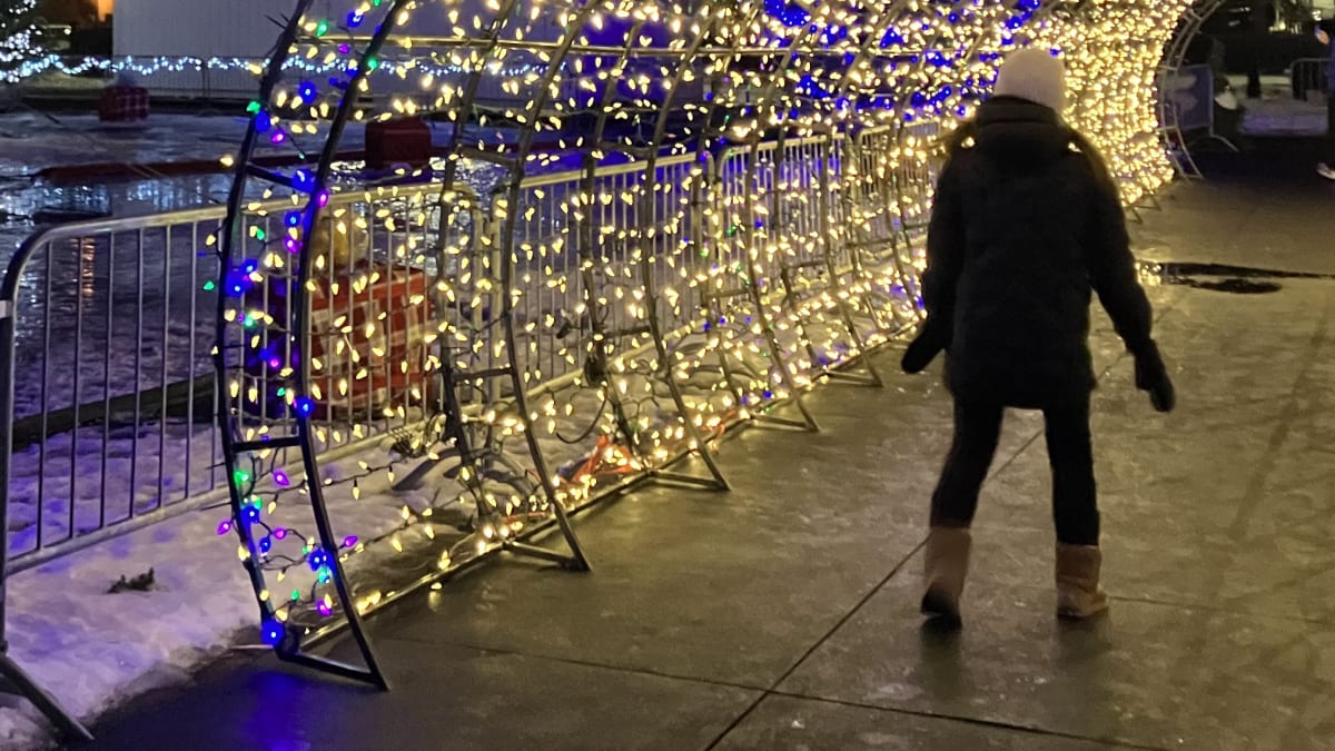 Woman walking under an illuminated arch outside.