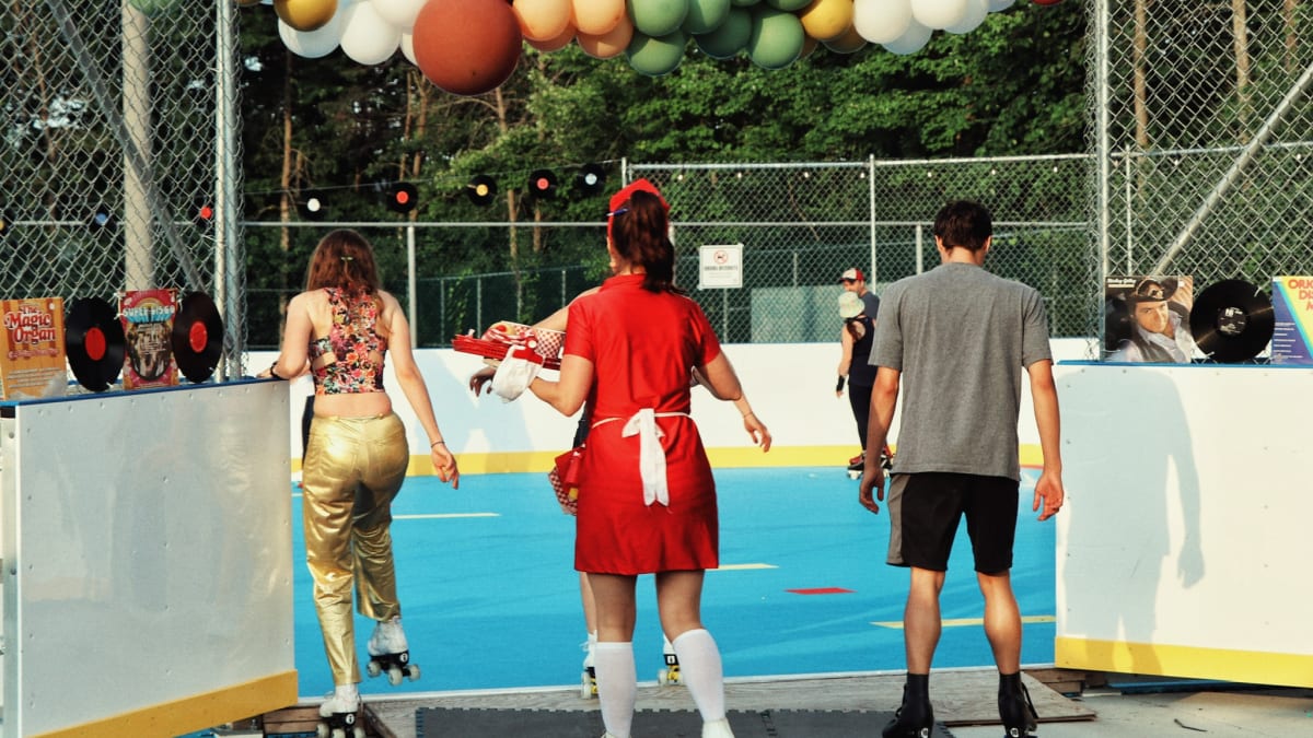 Three people on roller skates preparing to enter a rink decorated with balloons.