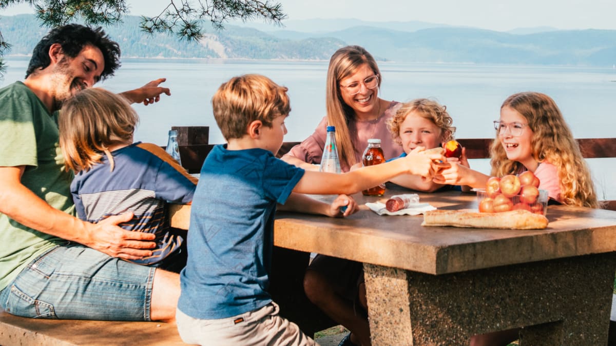 Family with young kids sitting around a picnic table next to the Saguenay Fjord.